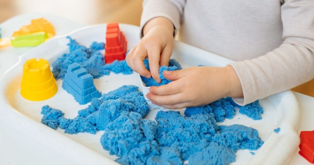 picture of a toddler playing with kinetic sand in a sensory bin